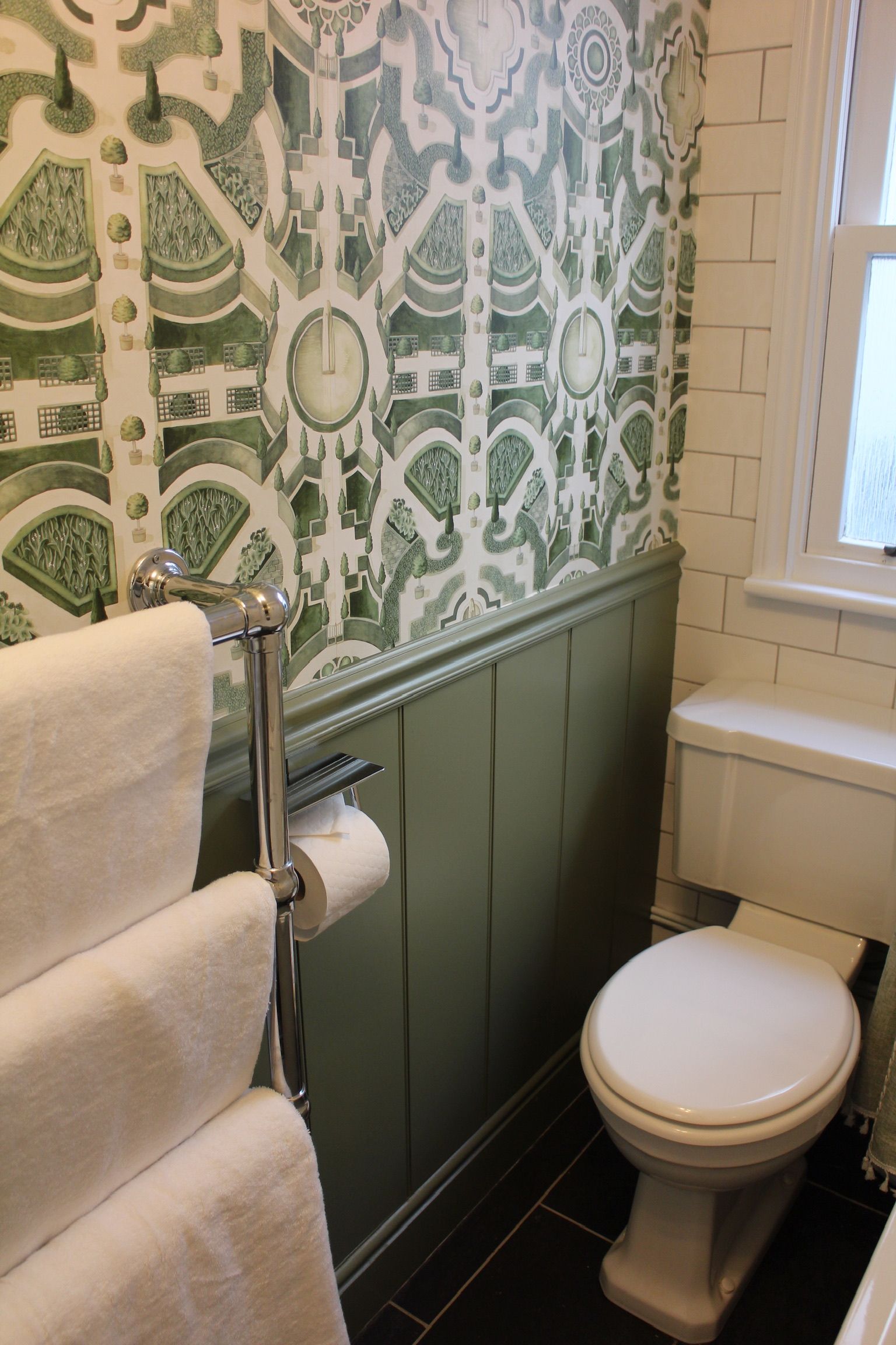 Een badkamer met een toilet, een handdoekrek en een behang met een patroon.