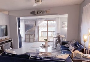 A living room with a sofa, coffee table, and a TV. There is a large window with curtains and a view of the outdoors.