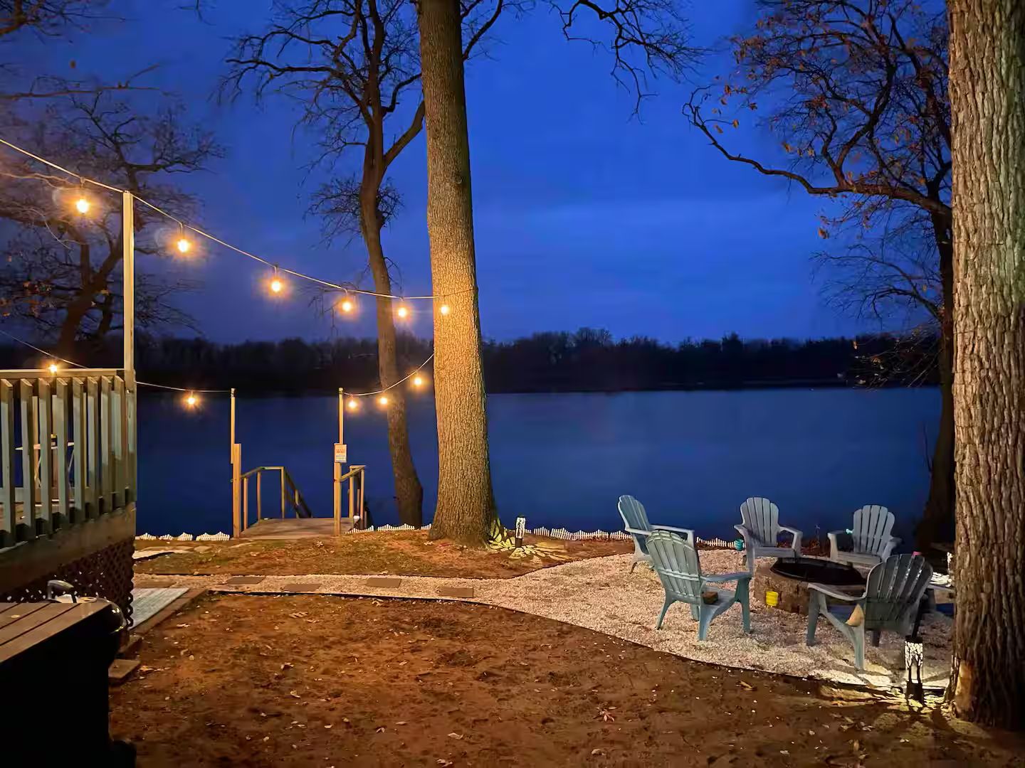 Una terraza junto al lago con luces colgantes, sillas Adirondack y barandilla de madera.