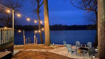 Una terraza junto al lago con luces colgantes, sillas Adirondack y barandilla de madera.