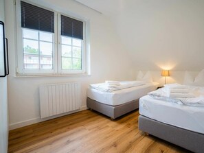 A room with two beds, a radiator, a window with blinds, and a lamp. - 10 in the Nis Randers House (St. Peter-Ording)