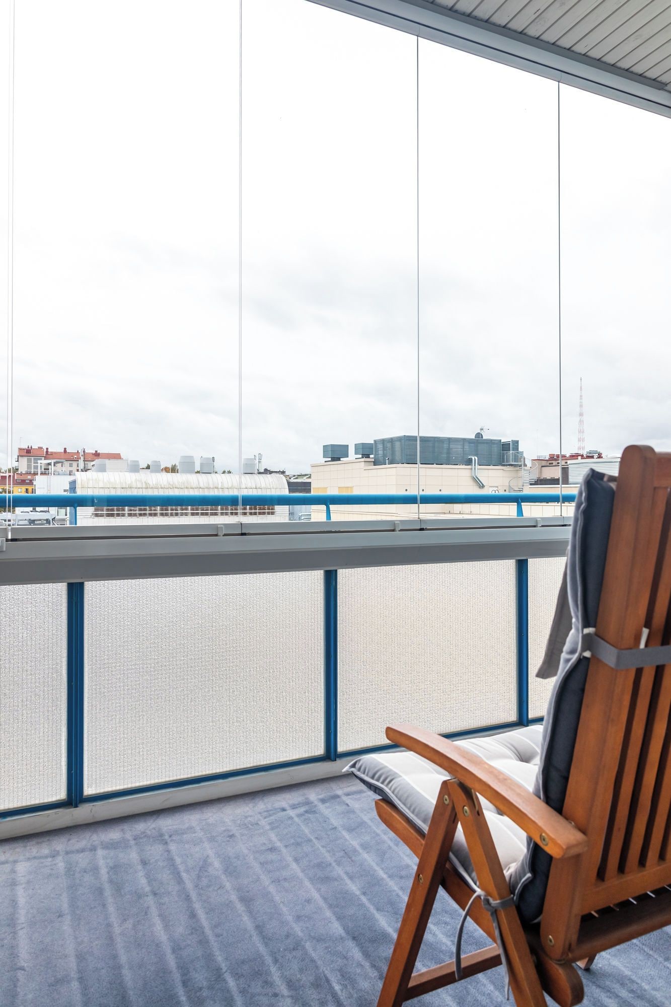 Ein Balkon mit einem Holzstuhl, Blick auf eine Stadtansicht und einer Brüstung.