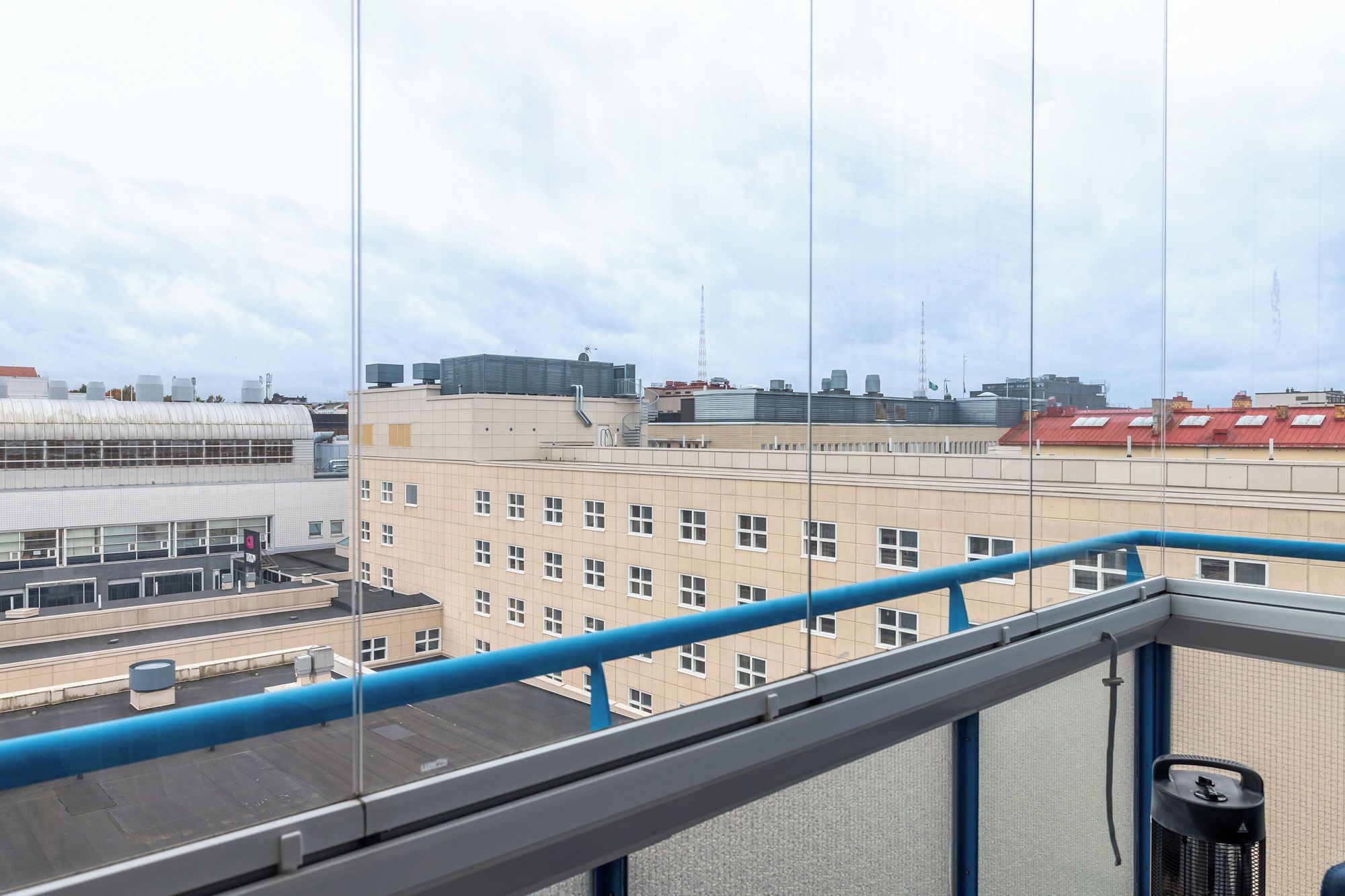 A view from a balcony with a blue railing, overlooking a building with multiple windows and a red roof.