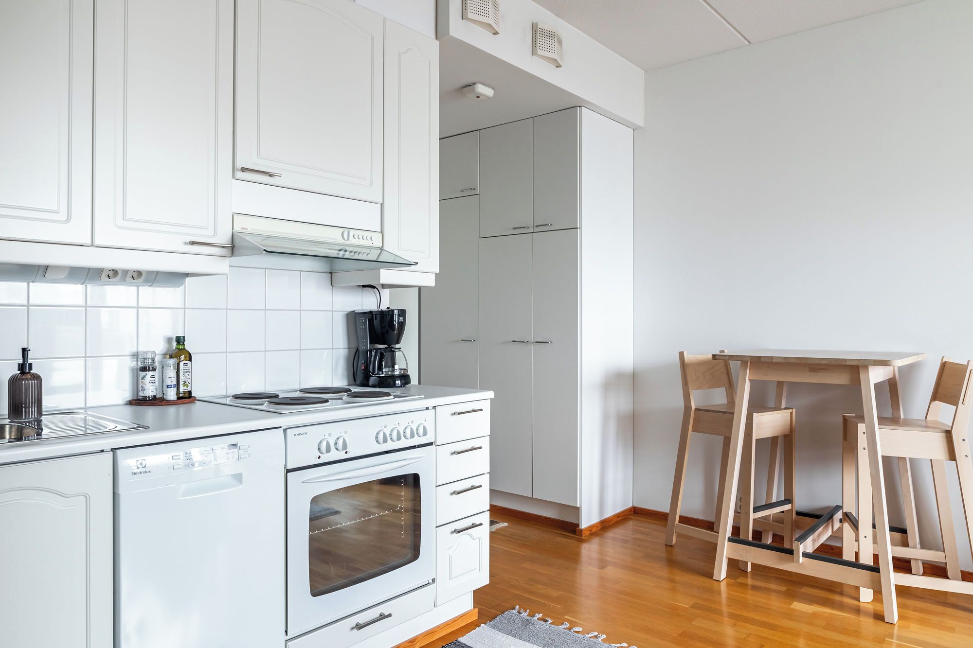 A modern kitchen with white cabinetry, a built-in oven, and a coffee maker.
