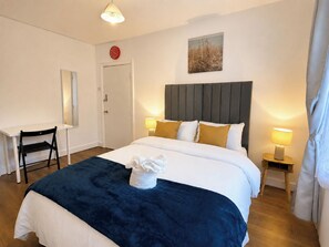 Ein Hotelzimmer mit einem Bett, Nachttischlampen, einem Schreibtisch, einem Sessel, einer Uhr und einem Bild an der Wand.