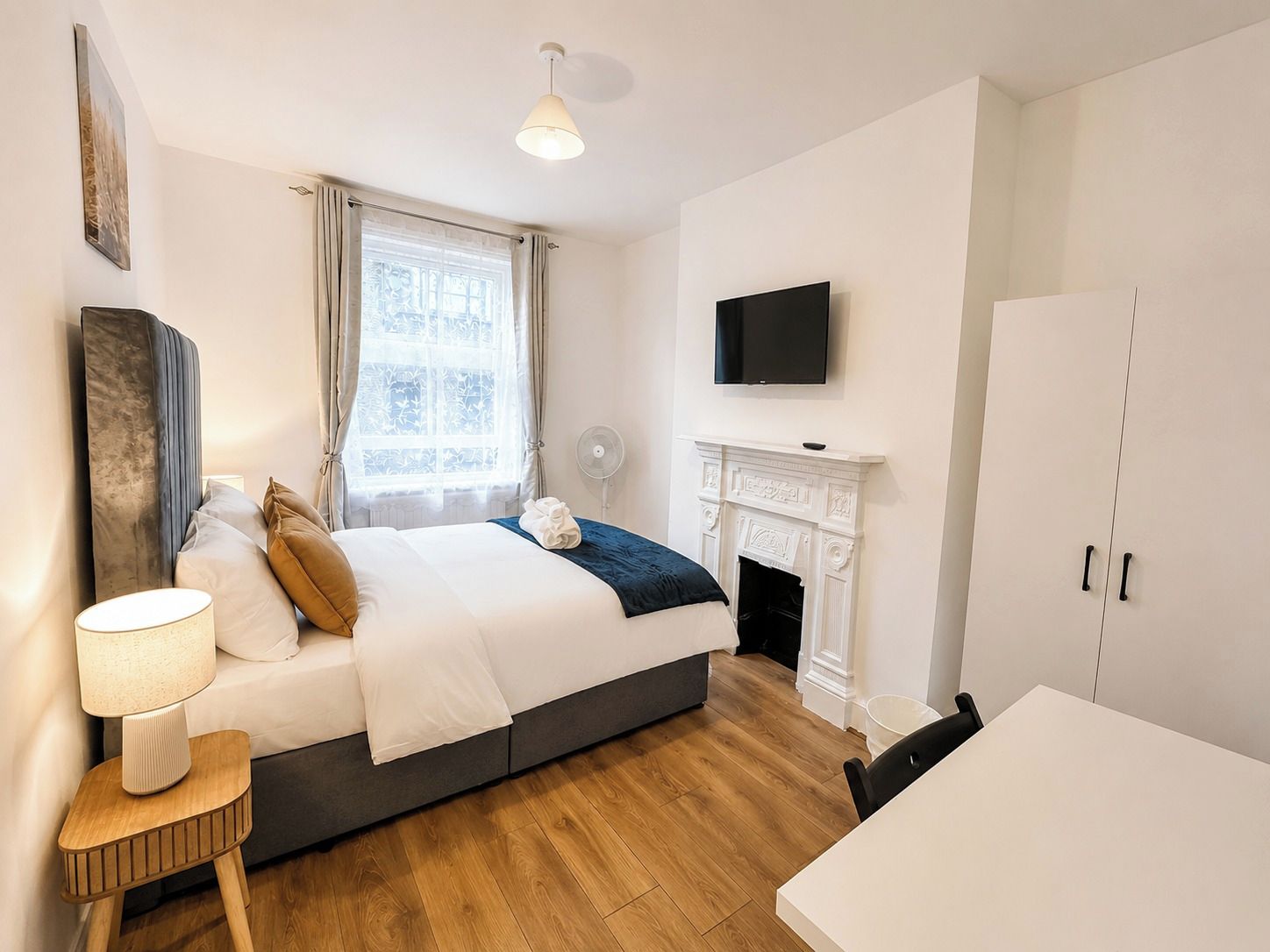 A bedroom with a bed, bedside table, lamp, TV, fireplace, and a dining area.