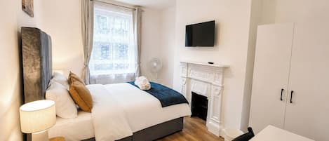 A bedroom with a bed, bedside table, lamp, TV, fireplace, and a dining area.
