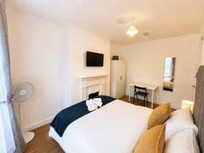Ein Hotelzimmer mit Bett, Schreibtisch, Sessel, Kamin, Fernseher und Spiegel.