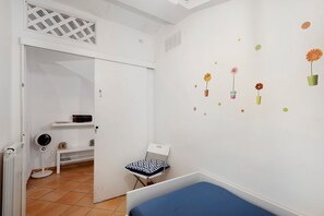 Habitación infantil con cama, una silla, un radiador y una puerta que da a otra estancia.