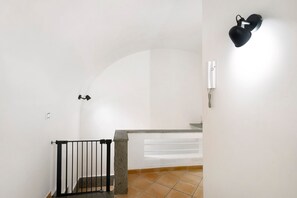 A staircase with a black railing, a stone pillar, and a white wall with a light fixture. - Enzo nel cuore di Napoli – Authentic Stay in Central Naples with Balcony (Napoli)