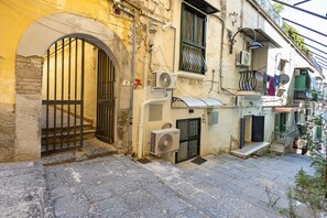 A narrow street with a building featuring a large arched entrance, a small balcony with a metal railing, and a satellite dish. - Enzo nel cuore di Napoli – Authentic Stay in Central Naples with Balcony (Napoli)