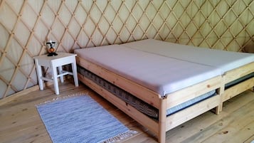 Una cama de madera con colchón y una mesita de noche blanca con lámpara.