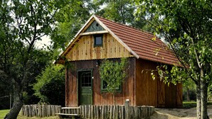 A wooden cabin with a green door, surrounded by a wooden fence, set in a grassy area with trees. - Őrálló Szer Jurtaszállás (Őriszentpéter)