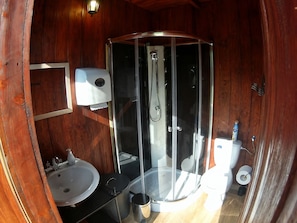 Ein Badezimmer einer Holzhütte mit einer gläsernen Duschkabine, einem Waschbecken, einer Toilette und einem Seifenspender.