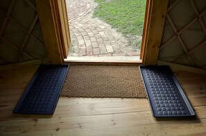 A room with a wooden floor, a doormat, and a view of a brick pathway leading outside.