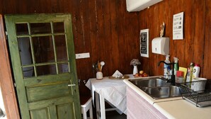 A rustic kitchen with a wooden door, a sink, and various kitchen items. - Őrálló Szer Jurtaszállás (Őriszentpéter)