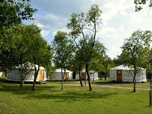 Jurten in einer grünen, baumgesäumten Gegend.