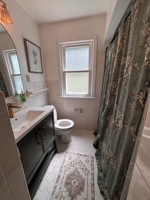 Ein Badezimmer mit einem weißen Waschbecken, einer Toilette, einem Fenster und einer Duschvorhang.