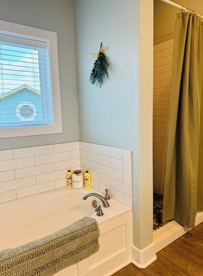 Ein Badezimmer mit einer weißen Badewanne, einem Fenster mit Jalousien, einem Duschvorhang und Pflegeprodukten am Waschbecken.