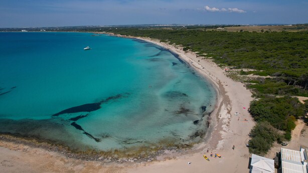 Luchtbeeld van een kustgebied met een strand, helder water en een jacht.