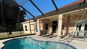 Piscina com água azul cristalina, rodeada por um espaço coberto com cadeiras e mesa.