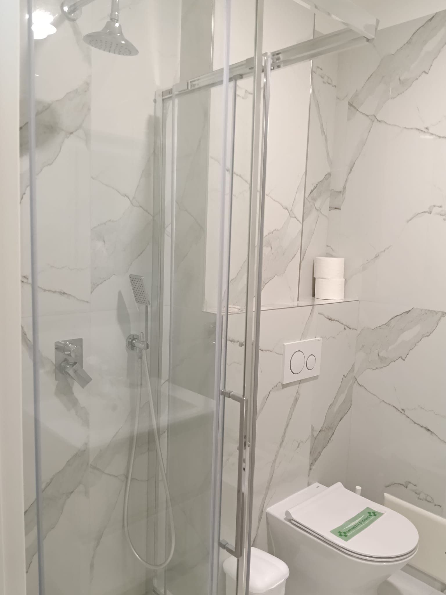 Une salle de bain moderne avec une douche à parois de verre, des toilettes et un mur décoré d’un motif imitant le marbre.
