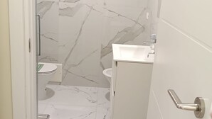 Ein Badezimmer mit Marmorboden, Toilette, Waschbecken und Duschbereich.