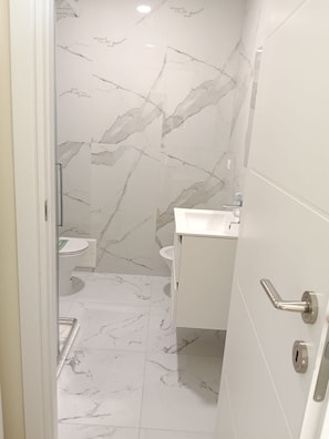 Ein Badezimmer mit Marmorboden, Toilette, Waschbecken und Duschbereich.