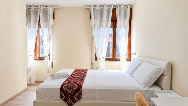 Ein Hotelzimmer mit einem Bett, einem Schreibtisch und zwei fensterbepflanzten Fenstern.