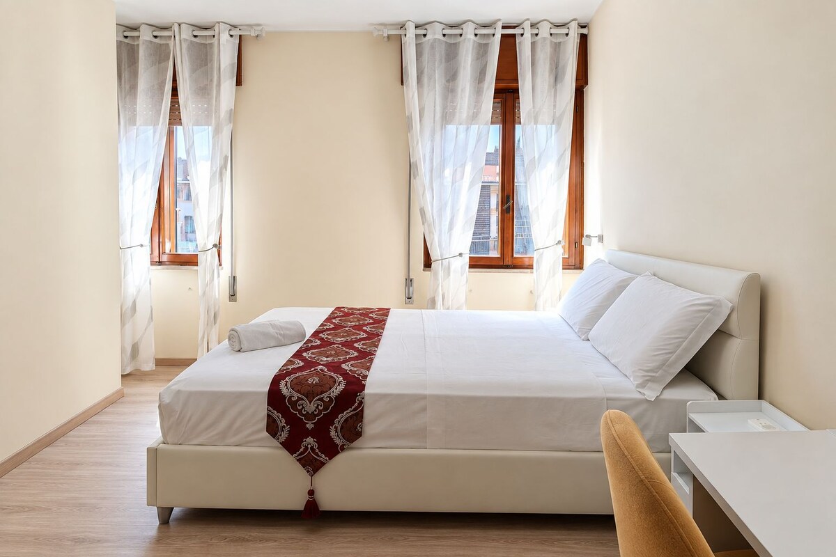 Ein Hotelzimmer mit einem Bett, einem Schreibtisch und zwei fensterbepflanzten Fenstern.