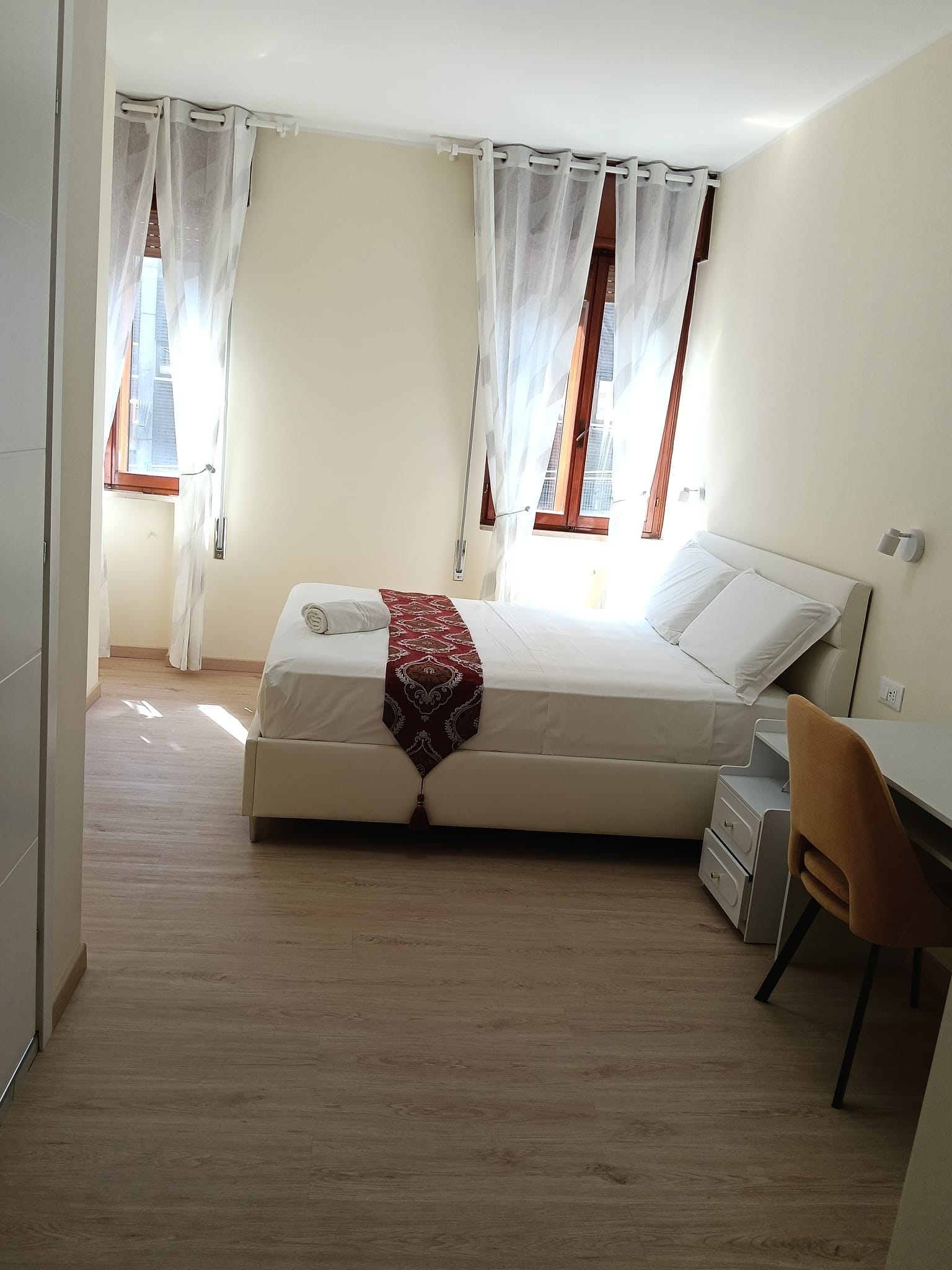 Une chambre à coucher avec un lit, un bureau et une chaise. Il y a des rideaux aux fenêtres.