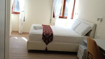 Une chambre à coucher avec un lit, un bureau et une chaise. Il y a des rideaux aux fenêtres.