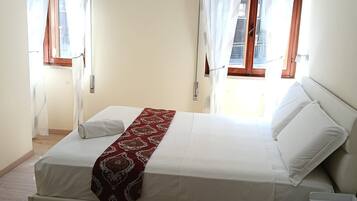 Une chambre à coucher avec un lit, deux fenêtres avec des rideaux, une table de chevet et une chaise.