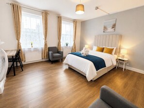 Ein Hotelzimmer mit Bett, Nachttischen, einem Sessel, einem Schreibtisch und einem fenster mit Vorhängen.
