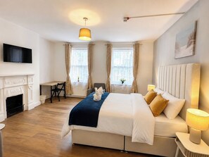 Ein Hotelzimmer mit Bett, Fernseher, Kamin, Schreibtisch und einem Fenster mit Vorhängen.