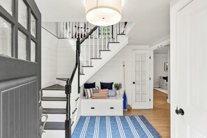 A staircase with a white railing, a blue rug, and a white bench with pillows. - The Creekhouse | Water Views | Lux Extended Stays (Portsmouth)