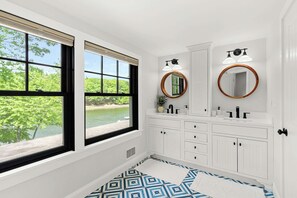 Ein Badezimmer mit großem Fenster, weißen Schränken, zwei Spiegeln und einem gemusterten Boden.