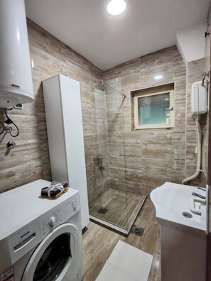 Une salle de bain moderne dotée d’une douche à parois de verre, d’un lave-linge encastré et d’un lavabo avec miroir.