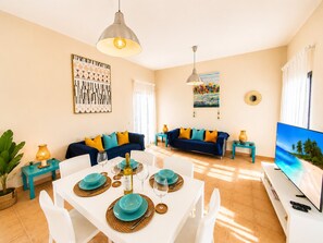 Ein modernes Wohnzimmer mit Essbereich, einer Sofagarnitur, einem Fernseher und Kunstwerken an den Wänden.