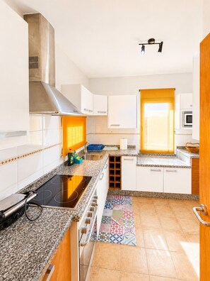 A modern kitchen with white cabinets, a stainless steel range hood, a built-in oven, and a colorful backsplash. - Nur house villa & private pool (La Oliva)