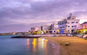A coastal area with buildings, a beach, and a body of water reflecting lights. - Alma Nomada Luxury Village & Private Pool & BBQ & ChillOut (Corralejo)