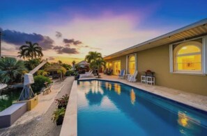 A swimming pool with lounge chairs and a covered area, surrounded by palm trees and a sunset sky. - Cudjoe Gardens Canal Front, Swimming Pool and Boat Lift (Cudjoe Key)