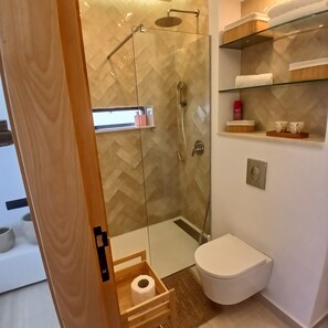 Ein modernes Badezimmer mit einer gläsernen Duschkabine, einer Toilette und einem Ablagefach für Toilettenartikel.