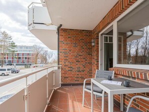 Ein Balkon mit Fliesenboden, einem weißen Metalltisch und einem Stuhl, sowie einer Ziegelwand.