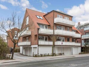 Ein mehrstöckiges Wohngebäude mit rotem Ziegeldach, weißen Balkonen und einer Garage.