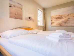Ein ordentlich gemachtes Bett mit weißen Leinen und einem Stapel gefalteter Handtücher.