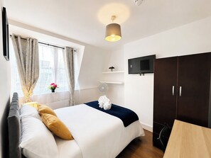 A hotel room with a bed, a desk, a wardrobe, a TV, and a window with curtains. - Double Room in East London near Aldgate East (London)
