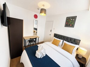 A hotel room with a bed, bedside table, lamp, and a desk with a chair. - Double Room in East London near Aldgate East (London)