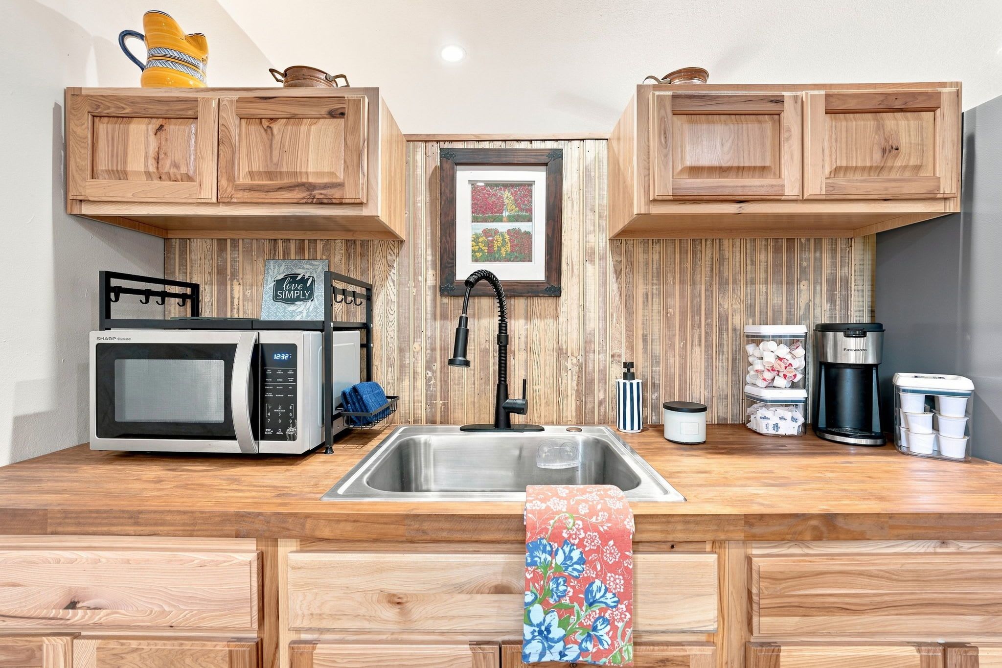 A compact kitchen with wooden cabinets, a microwave, a sink, and a coffee maker.