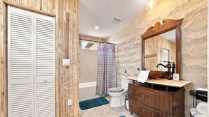 A bathroom with a wooden vanity, a large mirror, a toilet, and a shower area. - Buttons on the Pedernales Casita - Riverview (Stonewall)